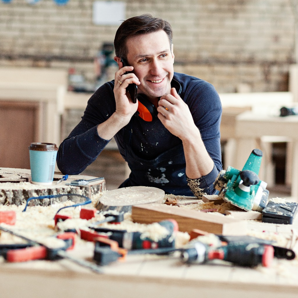 Smiling joiner talking on smartphone at workbench