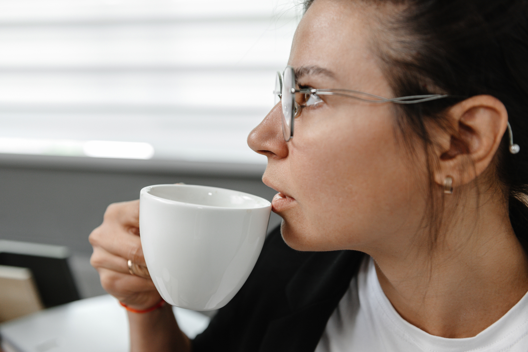 A girl drinks coffee in the office and thinks. A girl is thinking, a break in her work. The employee in the office is not smiling and drinking coffee