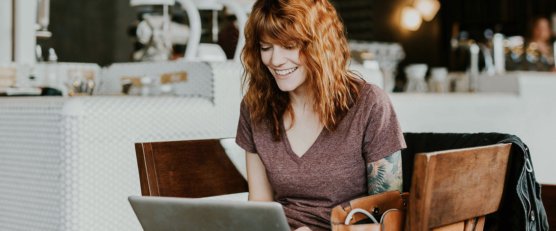 Frau mit roten Haaren sitzt in Café und arbeitet an Laptop